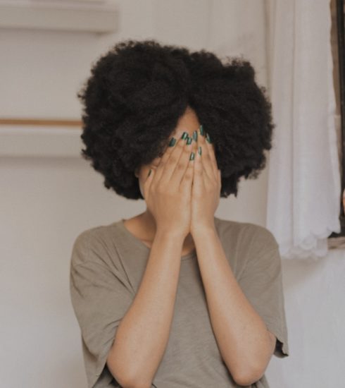 woman in gray t-shirt covering face with both hands
