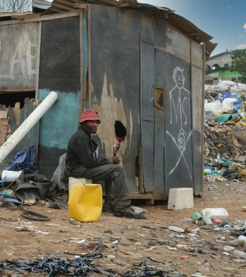 man in black jacket sitting on ground near garbage
